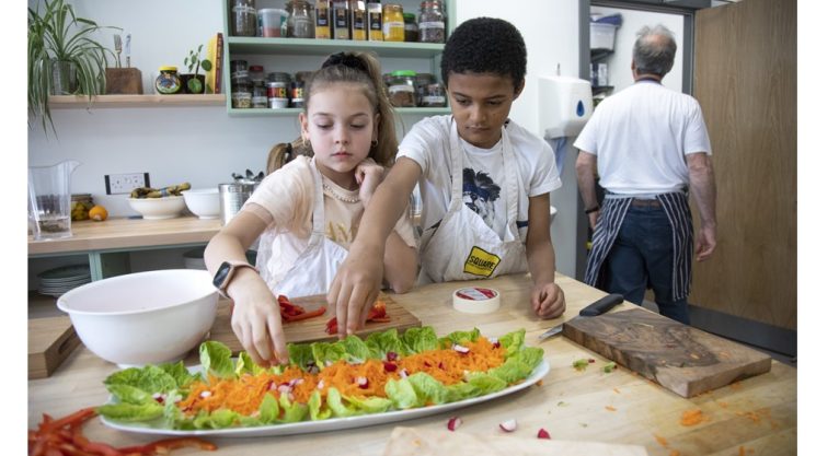 Picture of two children wearing aprons, preparing a colourful salad of lettuce, carrots and radishes. 